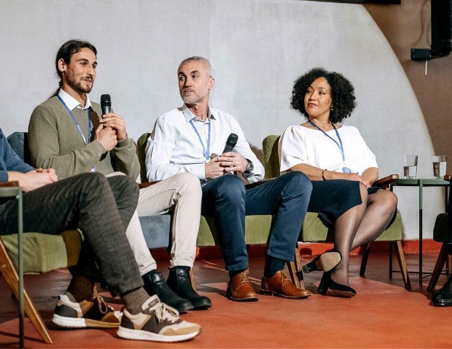 Panel med fem personer som diskuterar. Två män håller mikrofoner. De sitter i fåtöljer på en scen.