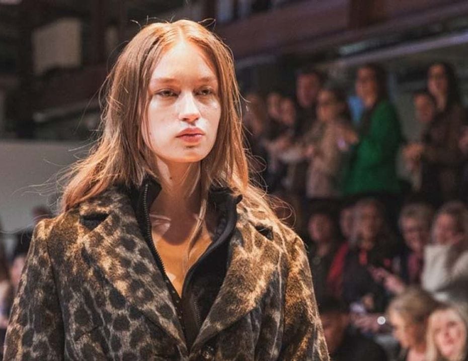 Modell på en modevisning för Trade Partners Sweden, klädd i en mönstrad jacka, medan åskådare sitter i bakgrunden.